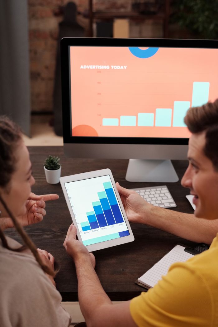 A group of coworkers in an office discussing sales growth while looking at a digital tablet and a computer screen.